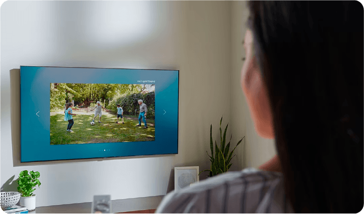 A woman watches a Samsung TV on the wall playing security footage of her backyard where her kids play.