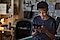 A young boy, looking down at and surfing on a black tablet as he sits on top of a desk in a garage.