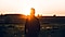 A man standing in a field looking towards the horizon as the sun rises.