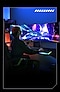 A woman is seen from the back, fully immersed in a game. Her right hand is placed on a mouse, which is on a mousepad that radiates blue-green lights. A horizontally placed Odyssey Ark Monitor is seen from the front and shows a spaceship dashing through a gateway. Blue-green beams are seen on the edges of the spaceship, indicating its interstellar speed. A moon and a few urban buildings are partially seen in the background.