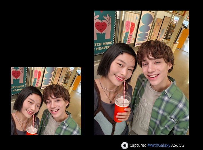 Two people smiling in a casual background. The person on the left is holding a disposable coffee cup. The angle implies they are taking a selfie. At the bottom is camera icon with text Captured by Galaxy A56 5G hashtag with Galaxy.