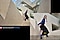 A photo of a woman standing on a staircase. Below, a zoomed-in photo shows the same woman with the staircase appearing larger. Text reads Captured by Galaxy S24 FE #withGalaxy.