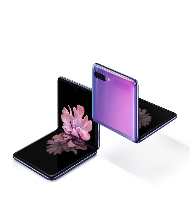 Two Galaxy Z Flip phones in Mirror Black at a three-quarter angle, one seen from the front and one seen from the rear. Both are folded at right angles with freestop folding. The one seen from the front has the blossoming flower wallpaper onscreen