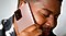 Khalid holds a Mystic Bronze Galaxy Note20 up to his right ear and closes his eyes, smiling. He's sitting on a beige couch and wearing a black and white tie dye t-shirt.