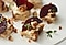 Group of bite-sized canapes with baked ricotta, beetroot wedges and caramel walnut brittle on it is on an white plate.