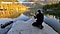 A rearview angle of Michael Block, kneeling on a rock, positioning a Galaxy S20 Ultra on a tripod at Grand Teton National Park. In front of him, there is a woman in a canoe on the water in front of tree-lined mountains.