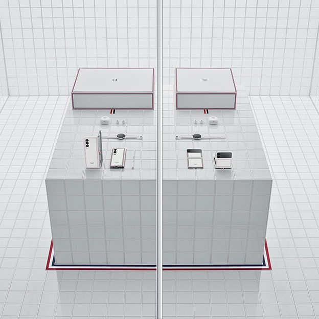 Hộp chứa Galaxy Z Fold3 và Galaxy Z Flip3 Thom Browne được đặt trên một chiếc bàn lát gạch trắng trong một căn phòng lát gạch trắng. Đường viền Thom Browne đặc trưng bao quanh bàn trên sàn nhà. Ở bên trái là hộp chứa Galaxy Z Fold3, gồm Galaxy Z Fold3, S Pen Pro, Galaxy Watch4, Galaxy Buds2 và vỏ hộp của tất cả các sản phẩm. Ở bên phải là hộp chứa Galaxy Z Flip3, gồm Galaxy Z Flip3, Galaxy Watch4, Galaxy Buds2 và vỏ hộp của tất cả các sản phẩm. Một bức tường chạy dọc xuống giữa màn hình, ngăn cách hai hộp chứa.  Logo hợp tác SAMSUNG - THOM BROWNE NEW YORK được hiển thị ở góc trên bên phải.