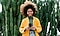 A woman with a bright coat and windblown hair stands in front of cacti and smiles at her Galaxy S21 Ultra.
