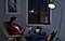 A woman reads in a chair next to a lamp in a dark room.