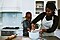 A woman and a young boy in the kitchen, preparing dough together on top of the counter. The woman is wearing a checkered apron.