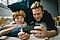 Father and son lay in bed on their bellies as the father holds a dark grey smartphone in landscape mode. Both the father and son smile as they gaze into the phone's display as if they're watching a show at home.
