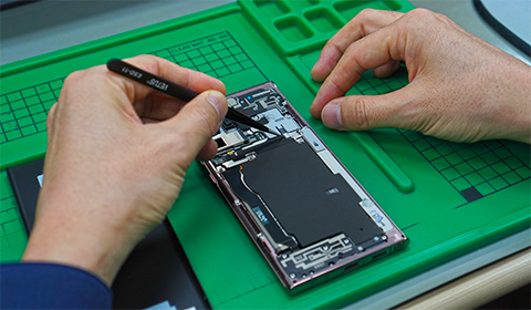 Closeup of the hands of a technician repairing a phone on a table. The phone has been taken apart with the interior components exposed