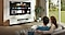 Duas pessoas sentam-se confortavelmente num sofá a ver o ecrã inicial do Smart Hub numa Smart TV Samsung elegantemente montada na parede.