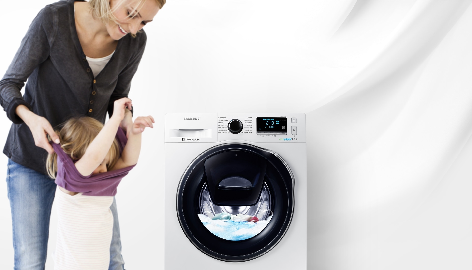 An image of a woman taking off her child's clothes next to a WW7500 washing machine which is in the middle of a cycle.