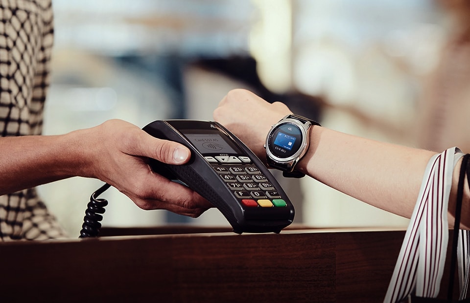 Woman extending wrist out to mst card payment machine to pay with Samsung Pay on her Gear S3