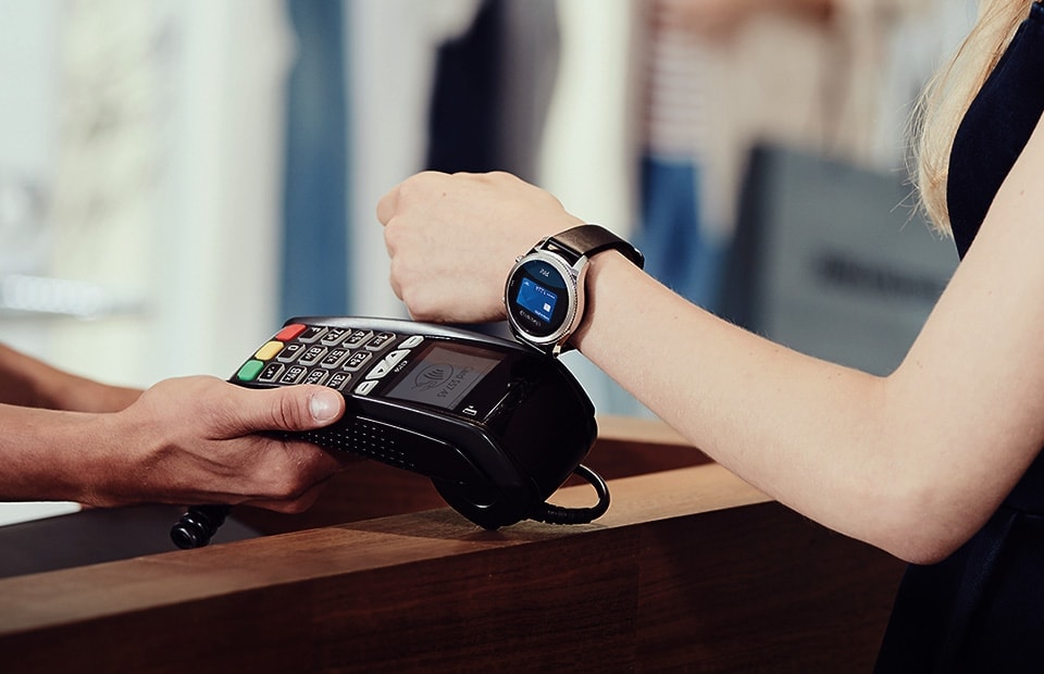 Woman extending wrist out to tap nfc card payment machine to pay with Samsung Pay on her Gear S3