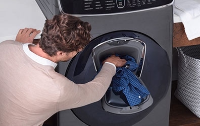 4. A man uses the AddWash door to insert a checkered shirt into the load of laundry. 
