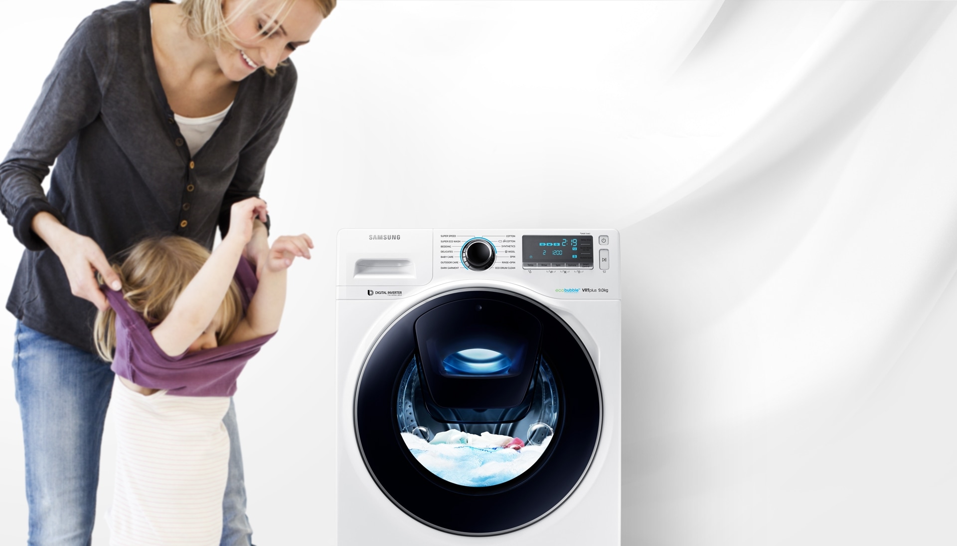  Un'immagine di una donna che toglie i vestiti del suo bambino accanto alla lavatrice WW7500 , che si trova nel mezzo di un ciclo di lavaggio.