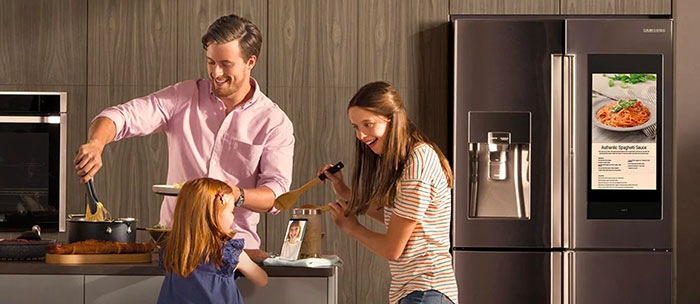 A family of three is seen happily cooking dinner in the kitchen together.