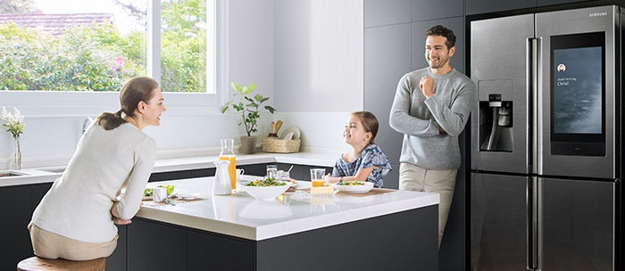 A family of three enjoys breakfast in the kitchen, while standing in front of the Family Hub refrigerator.