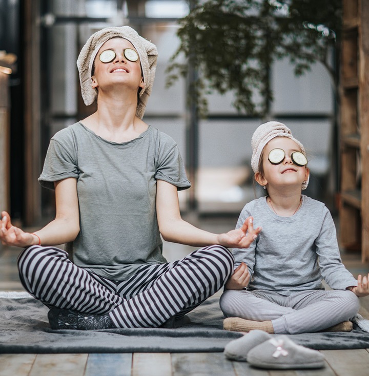 Mother and little girl taking care of their bodies in the morning while doing Yoga meditation exercises at home. Their hair is wrapped in towels while cucumber is on their eyes.
