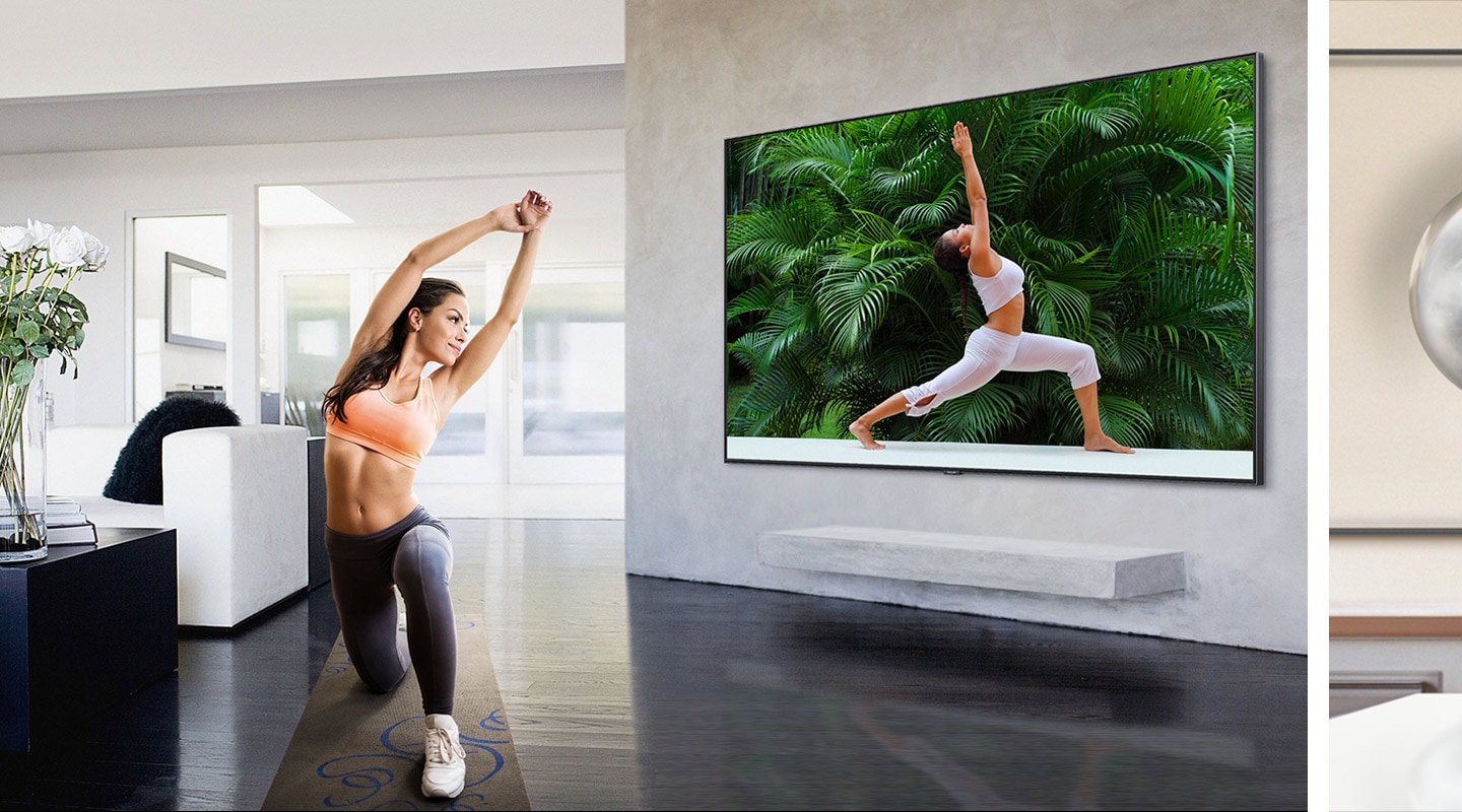 In a living room with white simple interior, a woman wearing a sportswear follows a yoga posture while watching a yoga training program on Super Big TV screen.