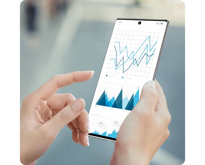 Hands holding Galaxy Note10+ with line graphs onscreen showing the uninterrupted view of the Infinity-O Display.