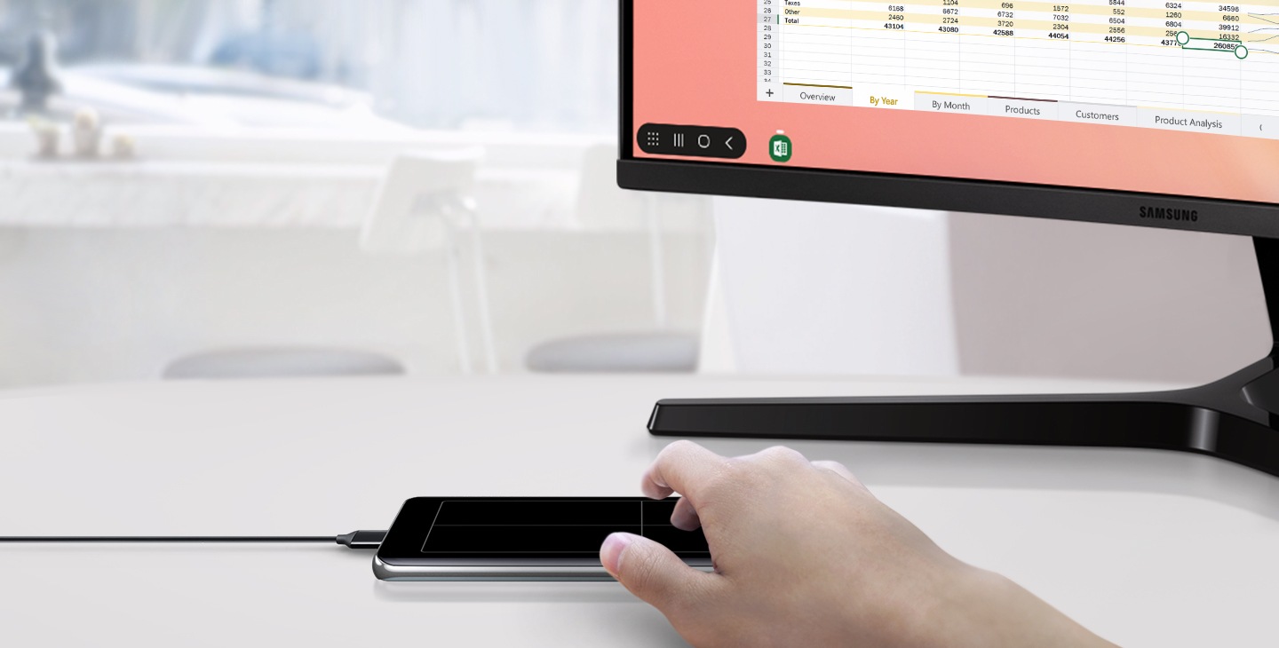 Image of Galaxy S10 plus connected to a monitor with DeX Cable and a person using the phone as a touchpad to work on a spreadsheet.