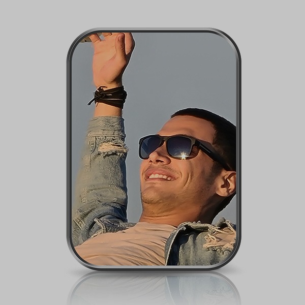 A closeup view of a man in sunglasses, smiling. His right arm is raised and outstretched to the sky.