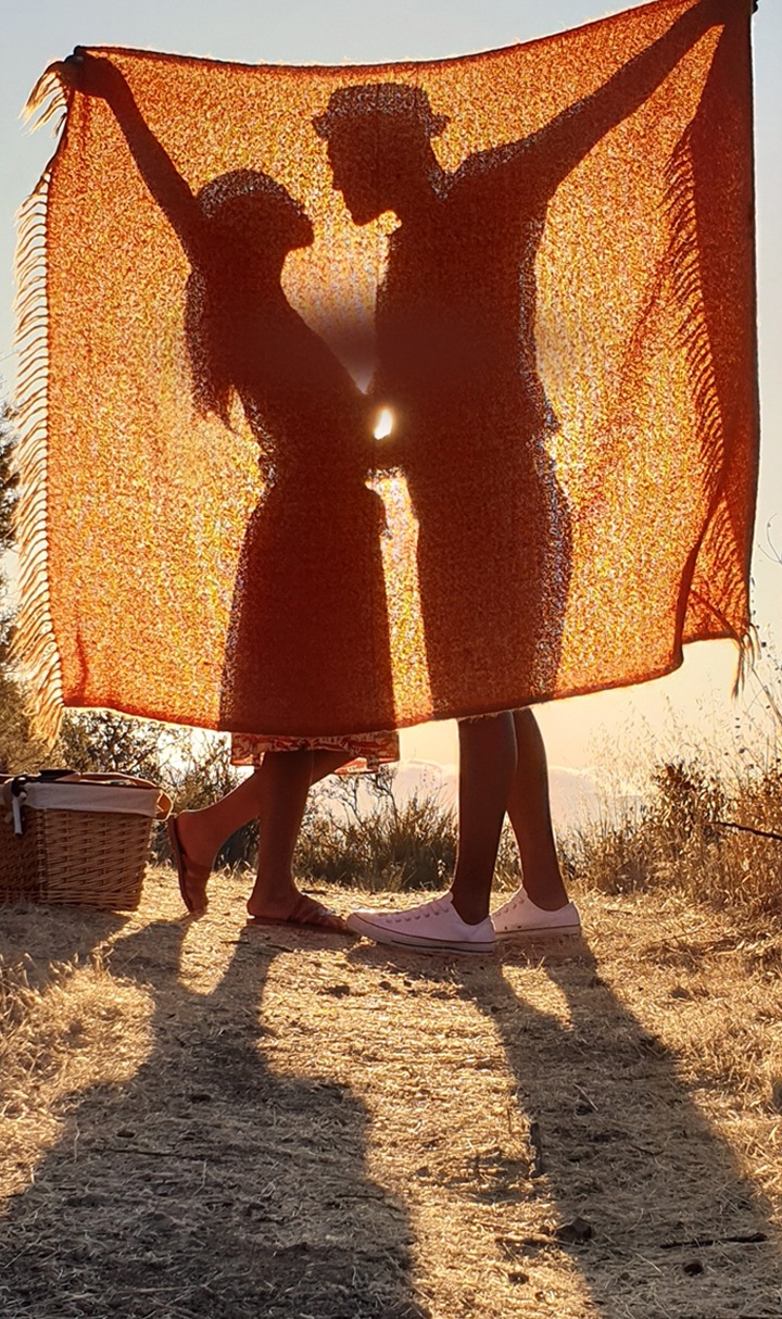 A photo taken by Galaxy Note9 of two people standing in a field behind a blanket with their shadows illuminated by the sun behind them