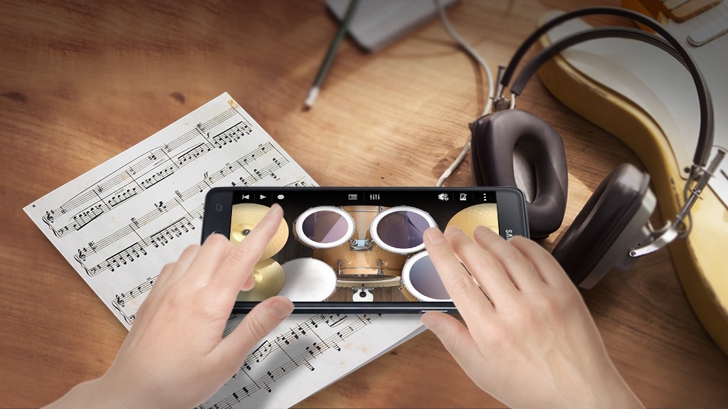 Imagem de uma pessoa a tocar bateria num Samsung Galaxy Note 4 com o Soundcamp em execução sobre uma imagem de fundo de auscultadores e uma pauta de música.