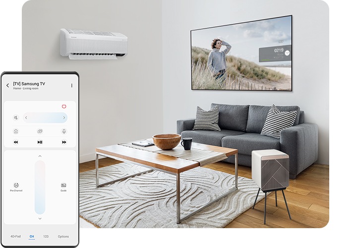 Uma sala de estar com um ar condicionado na parede e um Cube Air Purifier ao lado da mesa de centro, no meio da sala. Um sofá está atrás da mesa de centro e acima do sofá vê-se uma televisão QLED Q7 de 65 polegadas montada na parede. Em primeiro plano, do lado esquerdo, um ecrã de Galaxy mostra um controlo remoto num dispositivo móvel que controla a smart TV.