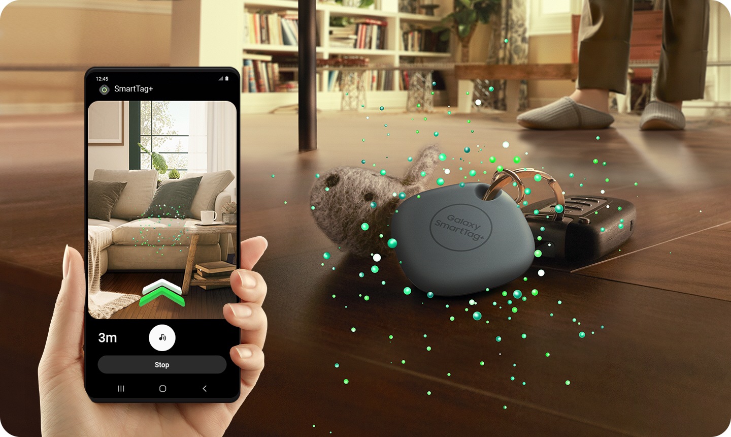 À esquerda, o ecrã de um smartphone Galaxy mostra uma imagem de um sofá e instruções que orientam para debaixo do sofá com bolhas esverdeadas que indicam de onde vêm os sinais da SmartTag+. Em segundo plano, uma SmartTag+ atada a um conjunto de chaves mostra que as chaves caíram para debaixo do sofá.