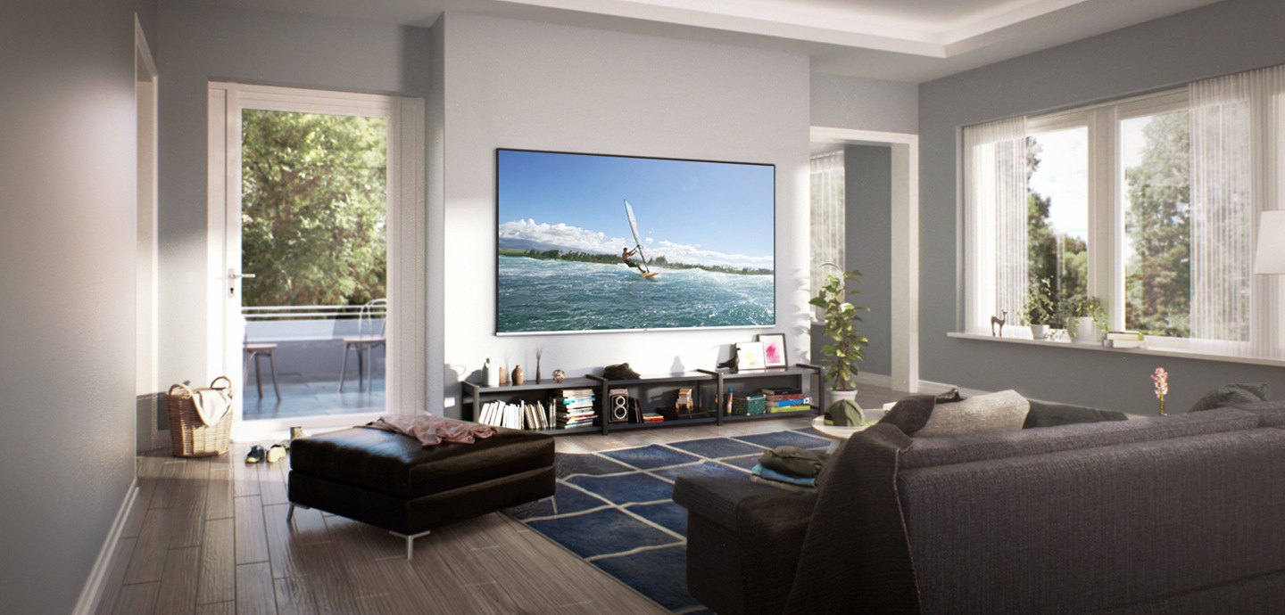 Visão ampla da acolhedora sala de estar com luz natural da janela. Uma TV super grande está pendurada na parede. No ecrã, um homem está a surfar.