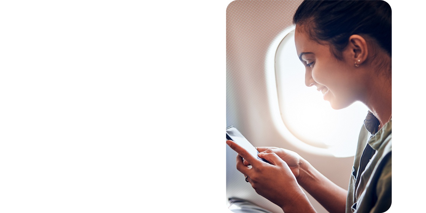 Vemos uma mulher sentada na janela de um avião a sorrir enquanto olha para o telefone.