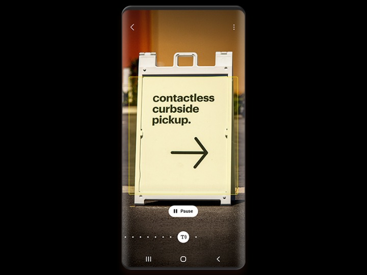 Një ekran telefoni tregon një tabelë me skelet A me tekstin "contactless curbside pickup", të identifikuar nga Bixby Vision dhe një buton pauze poshtë figurës.