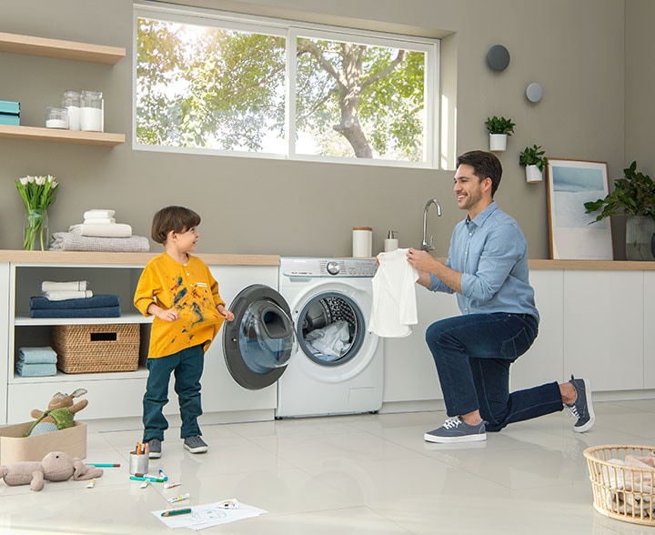 A father holding a white shirt with a kid in front of Samsung waching machine