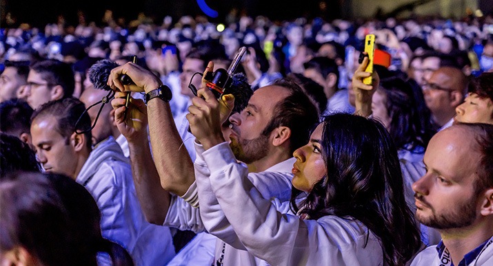 Au milieu d’une foule assistant à un évènement, une femme et un homme filment l’évènement avec leurs smartphones auxquels un micro est attaché.