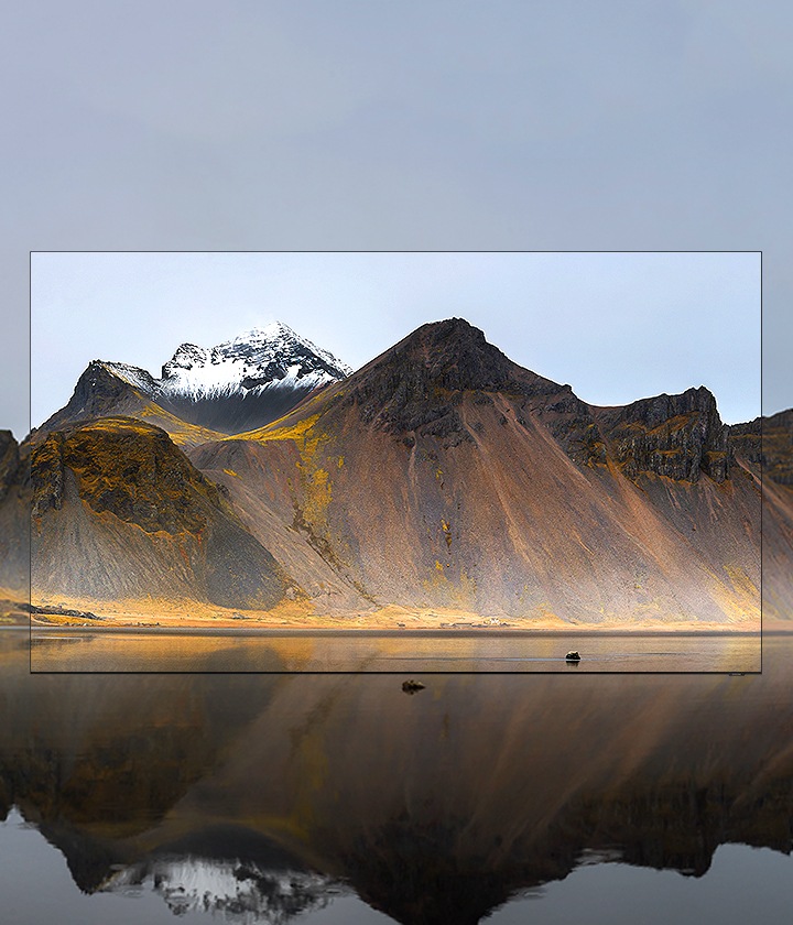 On voit une QLED TV au milieu d'un paysage montagneux. L'écran du Samsung QLED montre des montagnes, qui obscurcissent la vue sur les vraies montagnes. Mais grâce au design minimaliste et presque dépourvu de bords de QLED, le fameux Infinity Screen, les montagnes à l'écran se fondent parfaitement dans le véritable paysage de montagne.