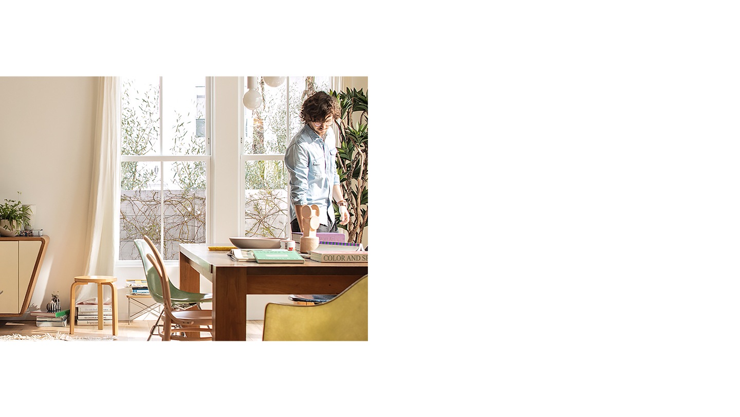 galerie 5 Un modèle Cloud White de la Serif est posé sans son support sur un buffet dans un intérieur design. L'image à l'écran est le Fabric Ambient Mode dans une couleur saumon. Un homme est en train de ranger la table.