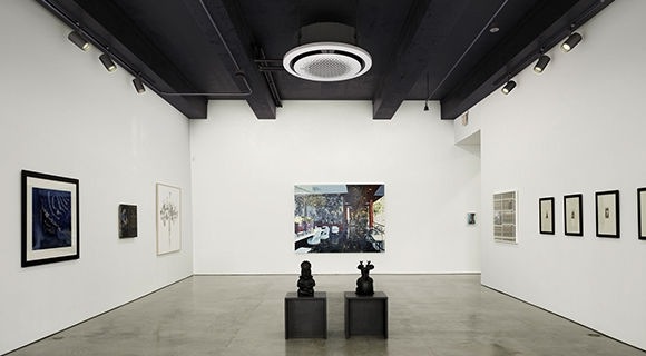 Imagem de um ar-condicionado da Samsung instalado no teto, no centro de uma sala de exposição de arte.