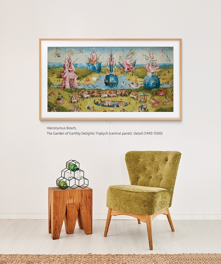 The Frame instalada em uma parede acima de uma cadeira estofada e mesa de canto geométrica com a moldura original do produto.