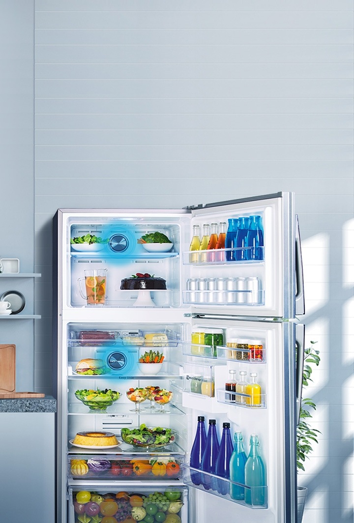 Refrigeradores Samsung Refrigerador Samsung Twin Cooling aberto com frutas, legumes e garrafas de água em um cozinha com um homem e duas mulheres sorrindo