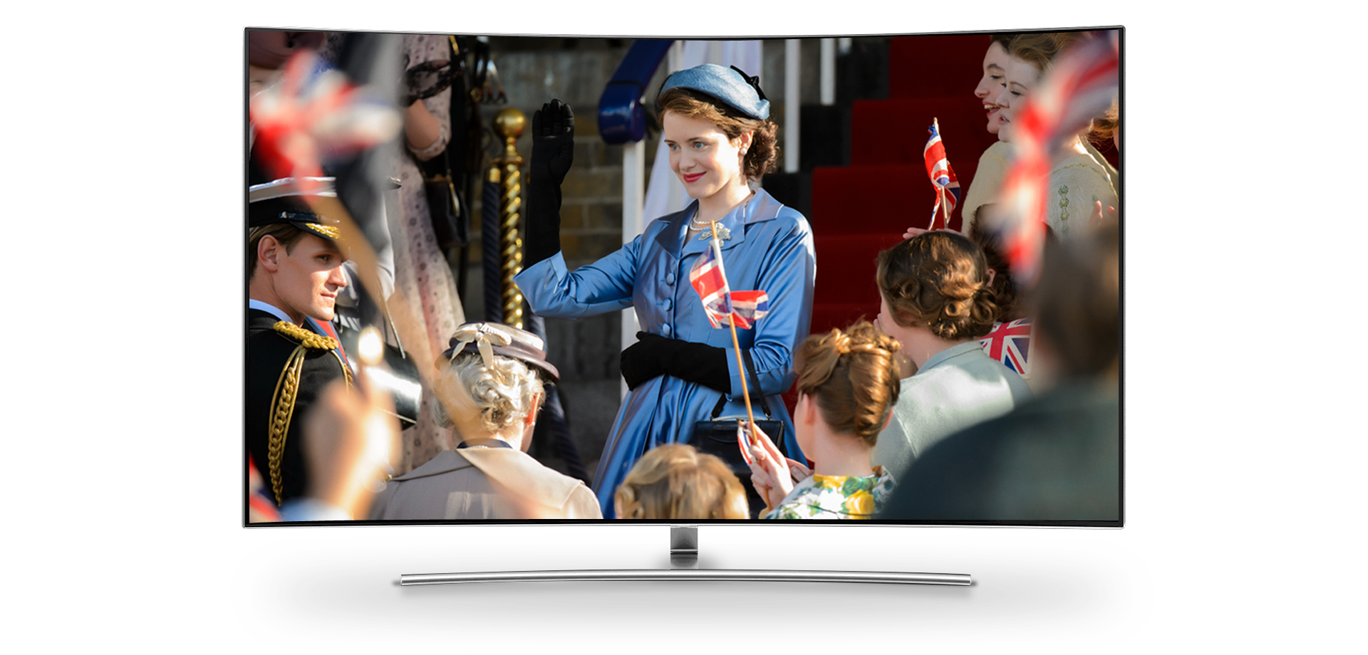 Cena da série The Crown. Uma mulher de vestido azul acena para um grupo de pessoas.