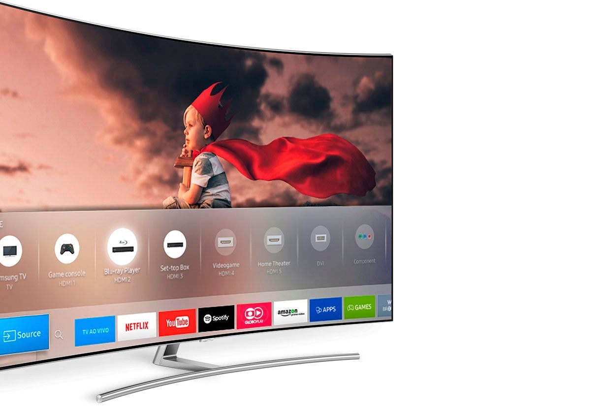 Smart TV Samsung em perspectiva lateral esquerda. Na tela, imagem de um menino com uma capa vermelha olhando para o horizonte. Abaixo dele alguns ícones como Joystick, Blu-ray Player HDMI, Samsung TV, entre outros.