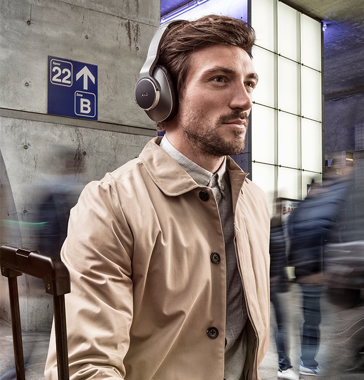 A man sitting in a busy waiting area, wearing AKG headphones