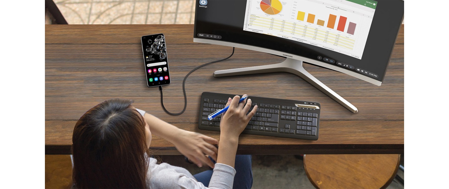 Une vue plongeante d’une dame assise à un bureau et travaillant à distance facilement en utilisant l’application DeX de Samsung pour connecter un appareil mobile à un écran d’ordinateur de bureau.