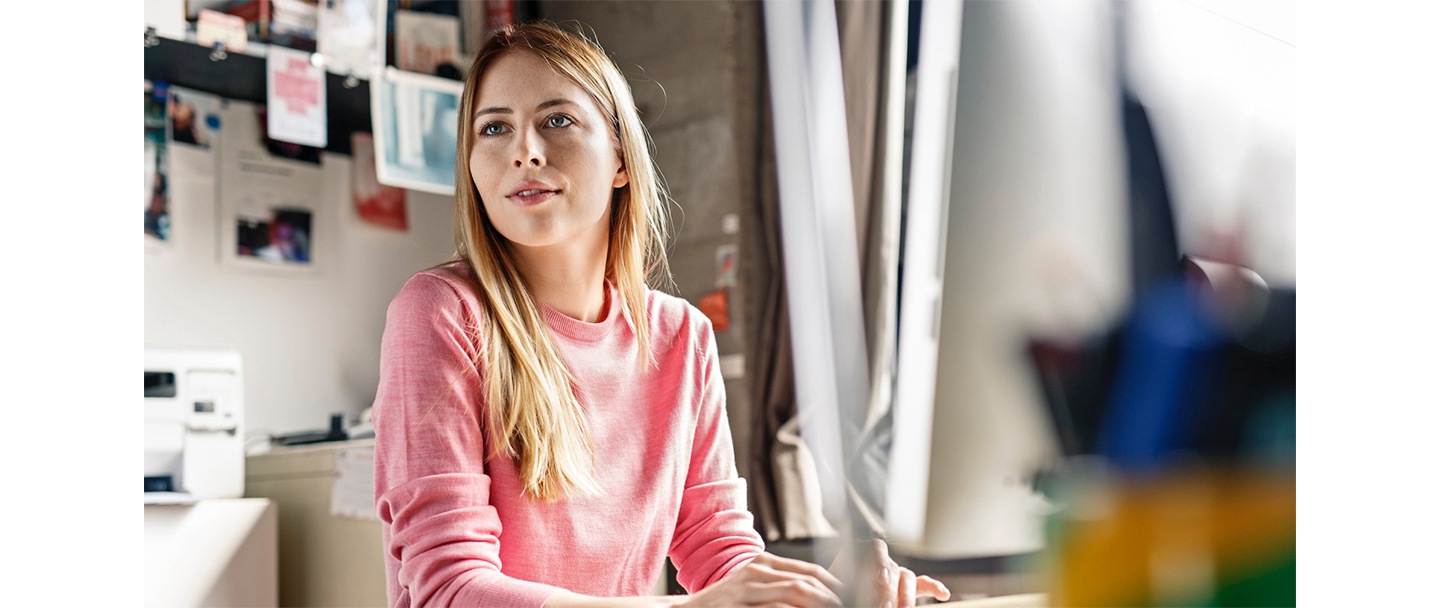 Une femme travaille à son bureau. Elle est assise devant un écran et ses doigts sont sur un clavier.
