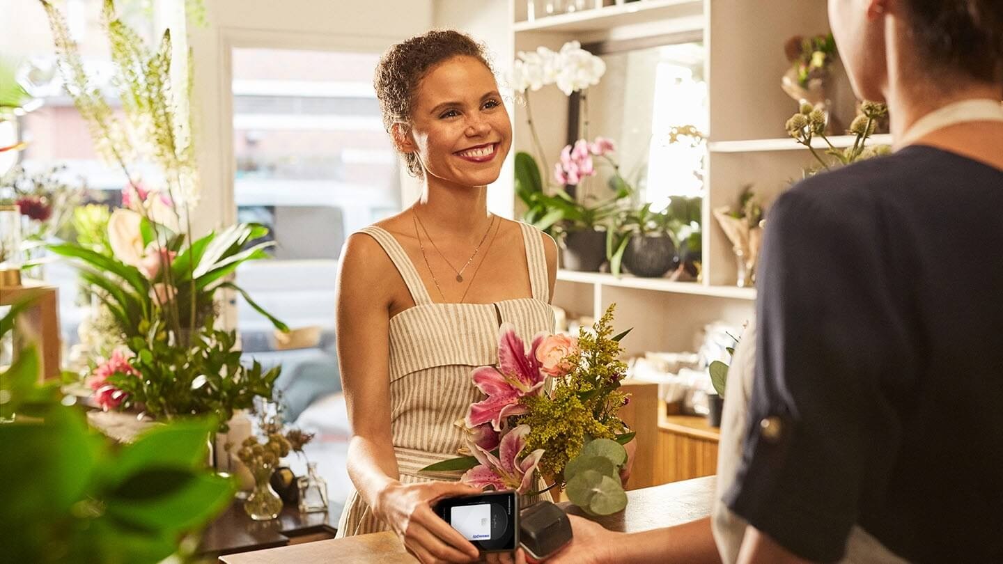 image d’une femme chez un fleuriste en face du caissier tenant un téléphone intelligent Galaxy au-dessus du terminal du point de vente du marchand et utilisant Samsung Pay pour effectuer la transaction.