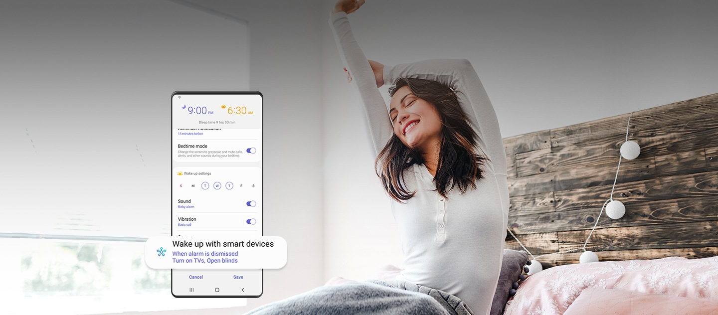 Une femme qui se réveille et qui s’étire sur le lit en souriant. Au premier plan, l'IUG d'un téléphone intelligent Galaxy indique la durée du sommeil et d'autres menus activés, notamment le mode Sommeil, le son, la vibration, etc. Vers le bas de l’IUG, un certain menu est agrandi. Il indique : « Réveillez-vous avec des appareils intelligents. Lorsque l’alarme est rejetée, allumez les téléviseurs et ouvrez les stores. »
